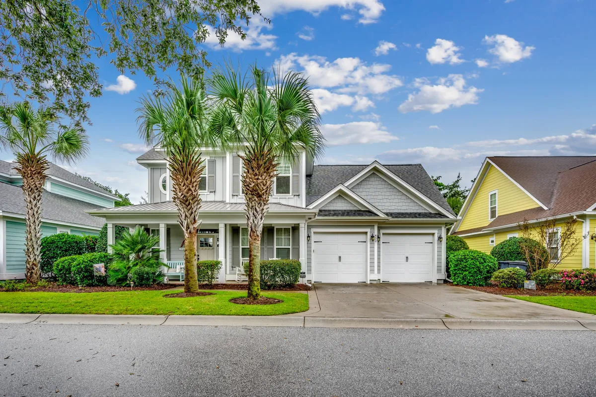 The image showcases a sunny, welcoming beach house framed by swaying palm trees, a wide front porch perfect for gathering, a spacious double garage, and a lush, landscaped garden. The inviting atmosphere suggests a relaxing, family-friendly space ideal for enjoying the coastal lifestyle.