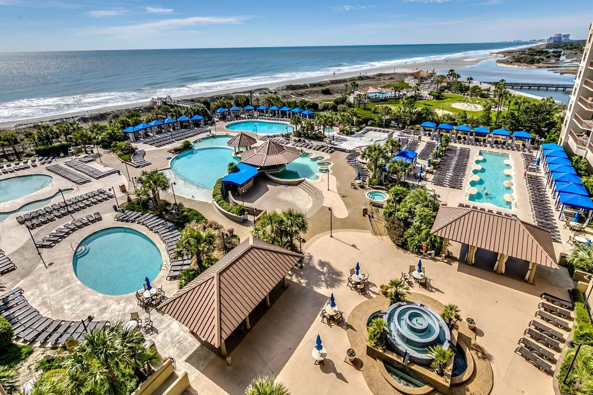A stunning exterior view of the resort’s pool complex, featuring several swimming pools surrounded by lounge chairs and palm trees. The beachfront location and a gazeebo add to the luxurious, inviting atmosphere for relaxation and social gatherings.