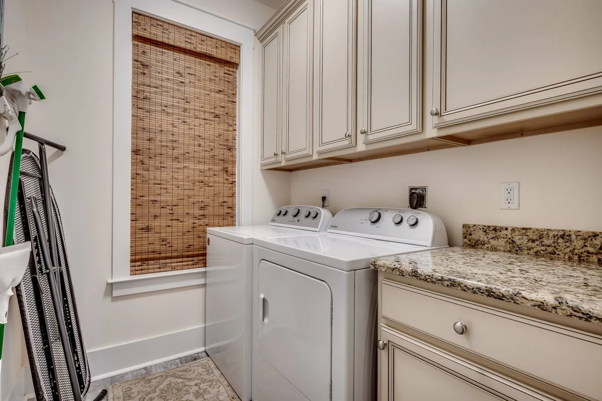 An organized laundry area equipped with a modern washer and dryer, granite countertop, and bamboo window shade, creating a practical space for keeping linens and clothes fresh during longer stays.