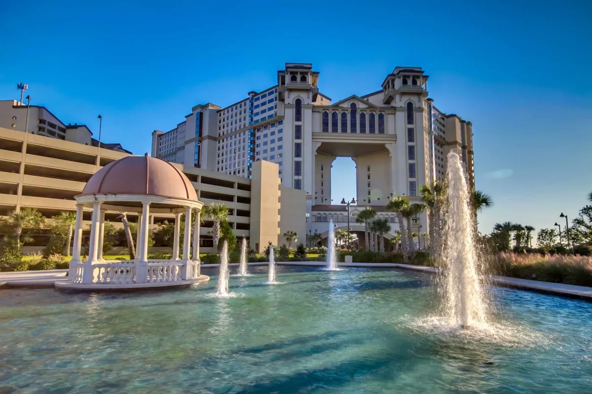A beautifully landscaped fountain area sits in front of a grand hotel building, with a charming gazebo nearby. The space is inviting and tranquil, offering opportunities for relaxing by the water or gathering with friends amid elegant architecture and landscaped gardens.