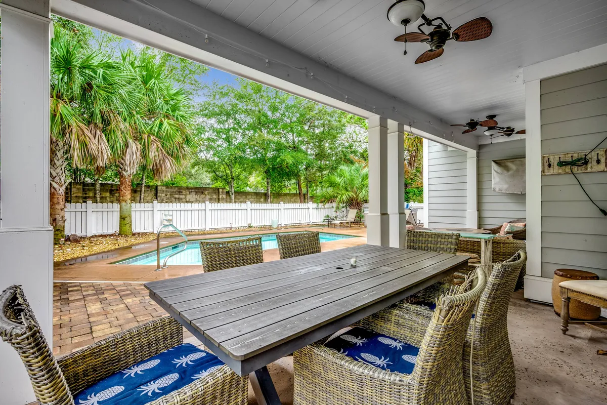 An inviting exterior dining area sits next to the sparkling pool, featuring a large outdoor table, cushioned seating, and overhead shade from palm trees. The setup is ideal for alfresco meals, family gatherings, or poolside barbecues under the sun or stars.