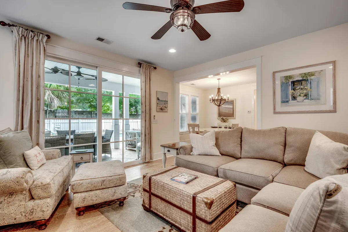 A cozy, welcoming living area with a comfortable sectional sofa, a decorative armchair, and a coffee table with magazines. Large sliding glass doors open to an outdoor space, blending indoor comfort with outdoor resort amenities.
