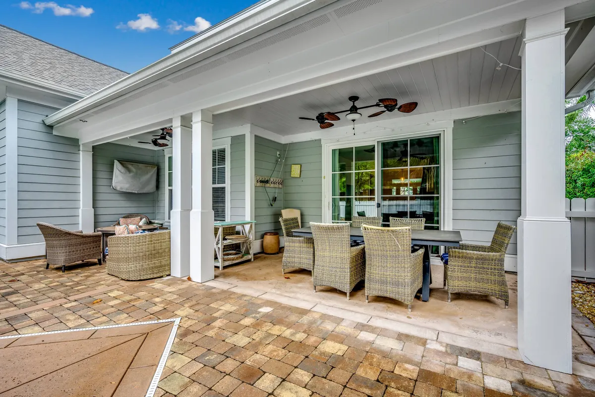 This inviting exterior shows a covered patio with wicker furniture, a dining table, ceiling fans, and large windows, all designed for outdoor relaxation and social gatherings. The view suggests a peaceful transition from action-packed days to comfortable evenings at home.
